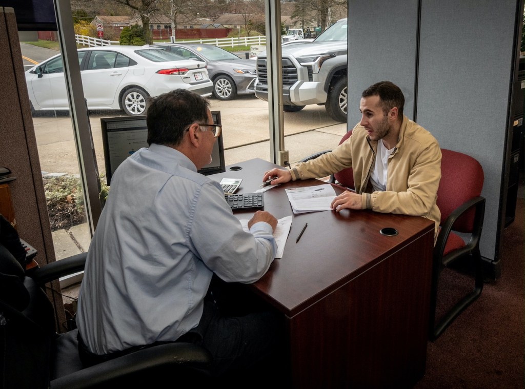 A car salesperson talks to a customer at his desk
