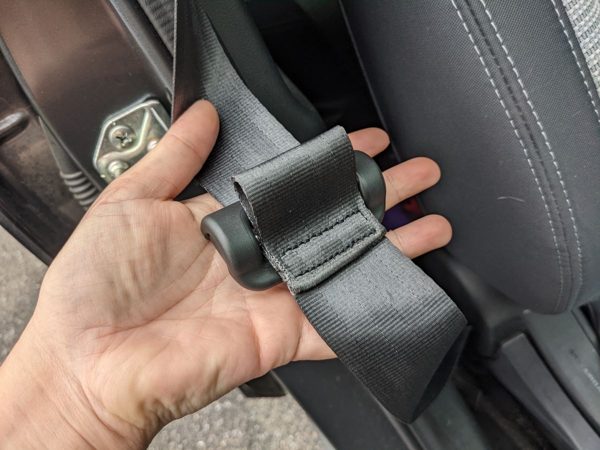 A hand holding the buckle and energy management loop portion of a Subaru Outback's seat belt