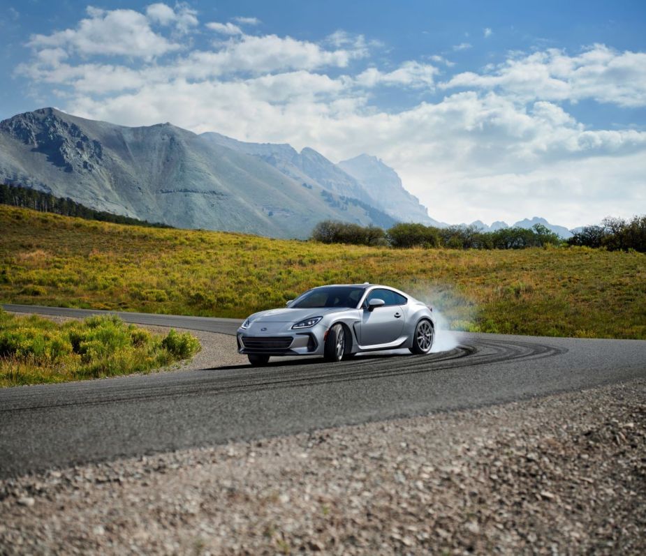 Silver 2022 Subaru BRZ two-door sports car drifting on a curved road with gorgeous mountains in the backdrop. This model is a big step in the Subaru BRZ's history