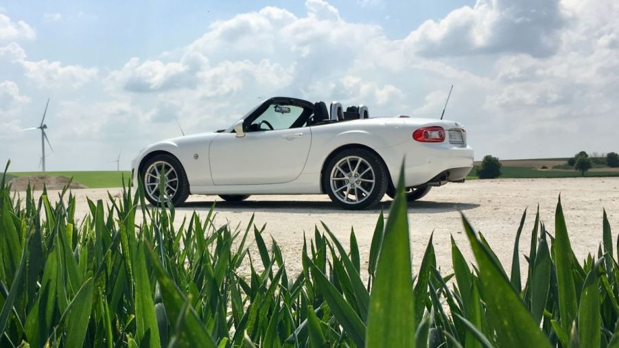 White Mazda Miata parked on a sunny road with bright green grass in front of the