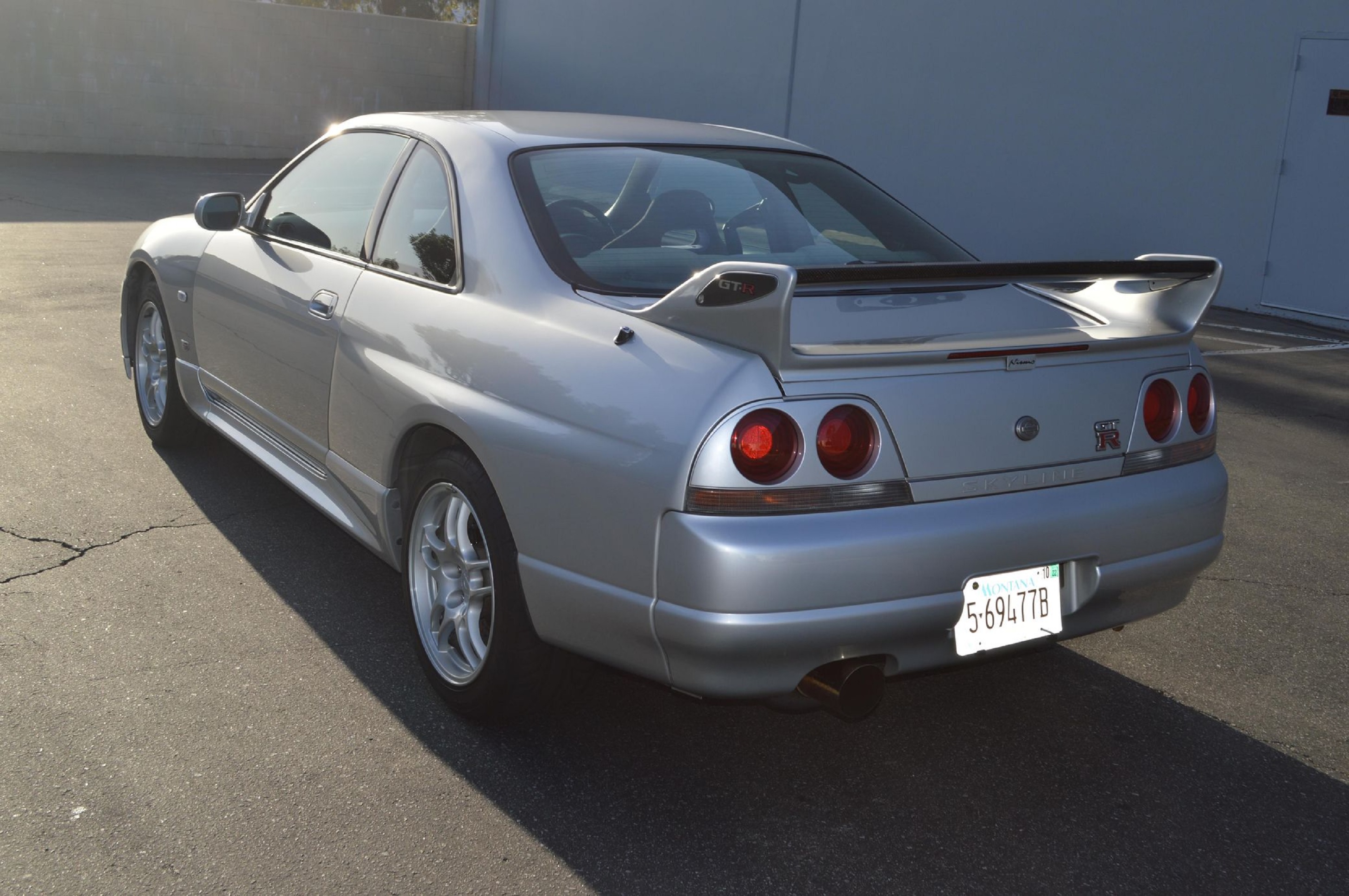 The rear 3/4 view of a silver 1995 Nissan R33 Skyline GT-R in a parking lot