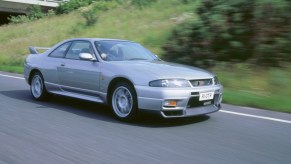 A silver 1998 Nissan R33 Skyline GT-R driving down a road at speed