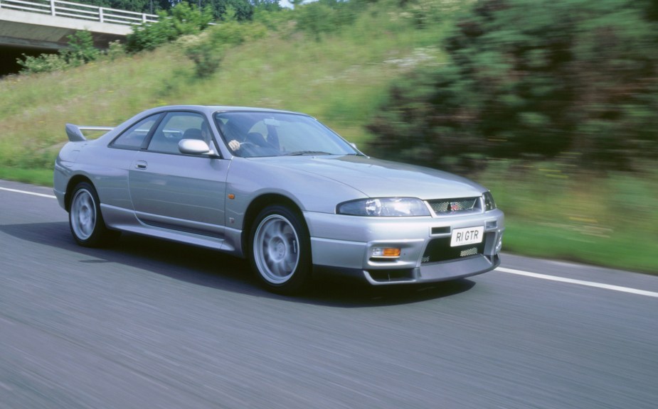 A silver 1998 Nissan R33 Skyline GT-R driving down a road at speed
