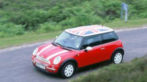 A red 2002 R50 Mini Cooper with a Union Jack flag roof decal drives down a country road
