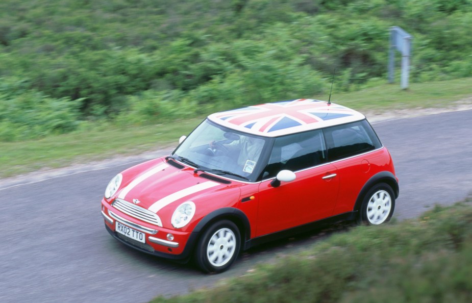 A red 2002 R50 Mini Cooper with a Union Jack flag roof decal drives down a country road
