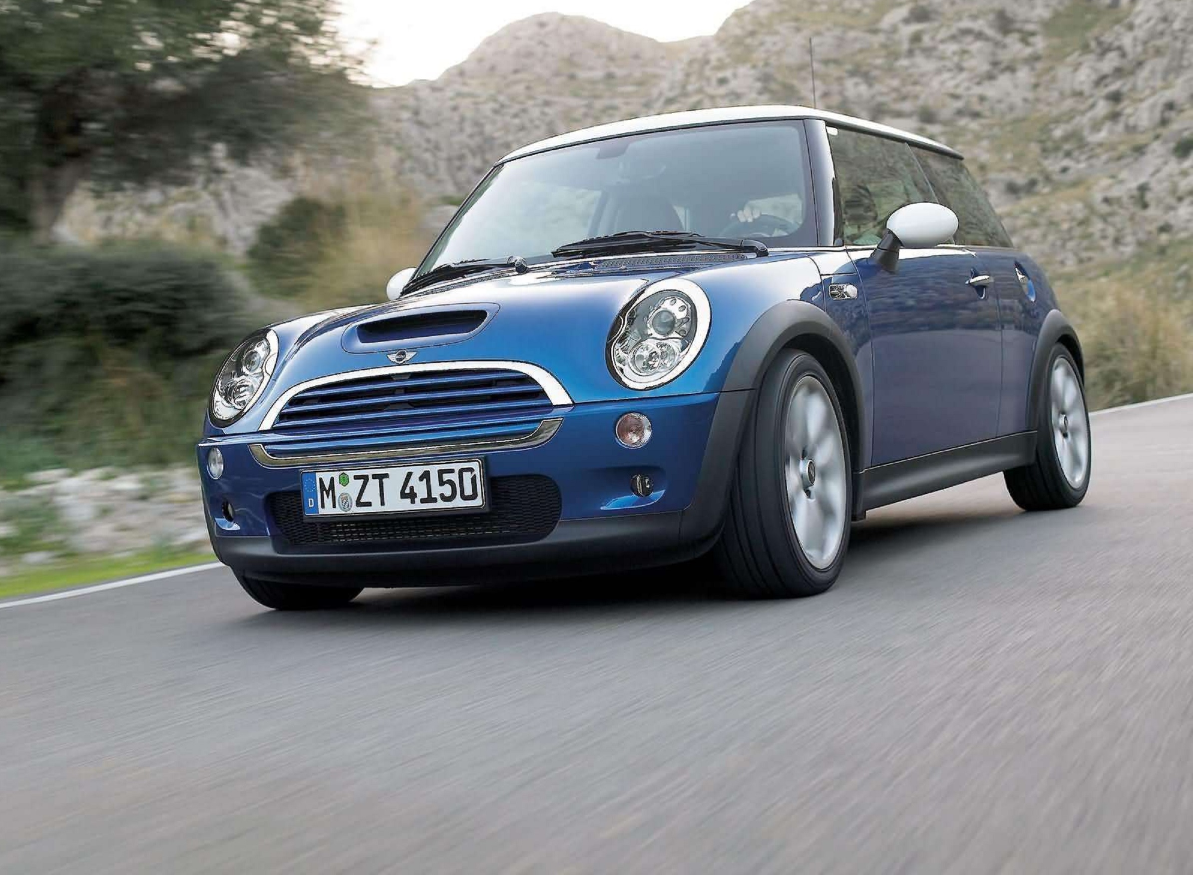 A blue 2005 R53 Mini Cooper S driving on a desert canyon road