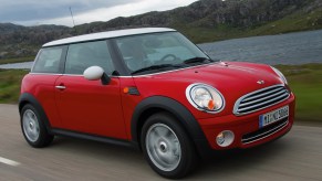 A red 2007 R56 Mini Cooper driving down a road next to a hillside lake