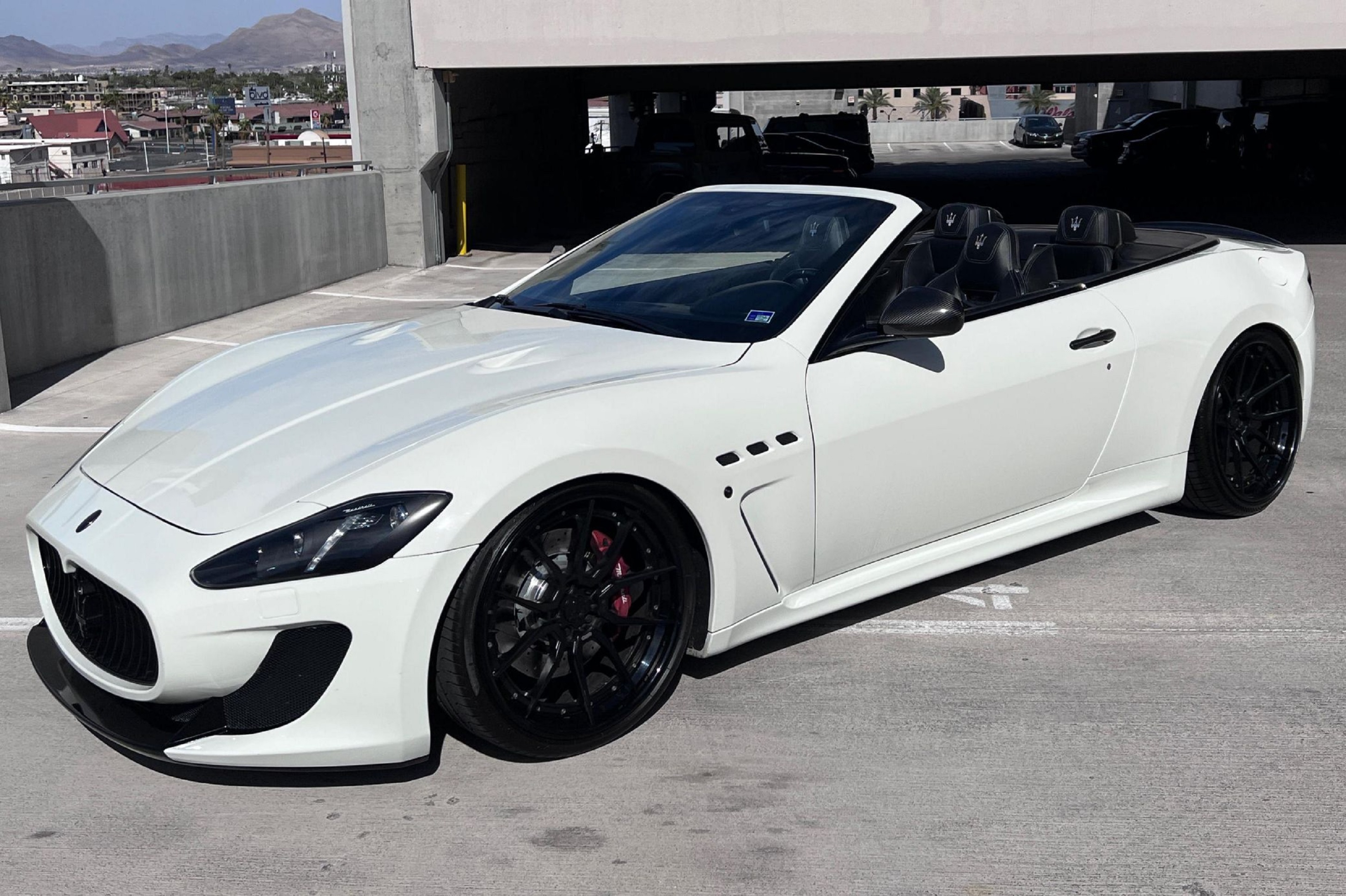 A 2013 white Maserati GranTurismo MC Convertible on black aftermarket wheels in a parking garage