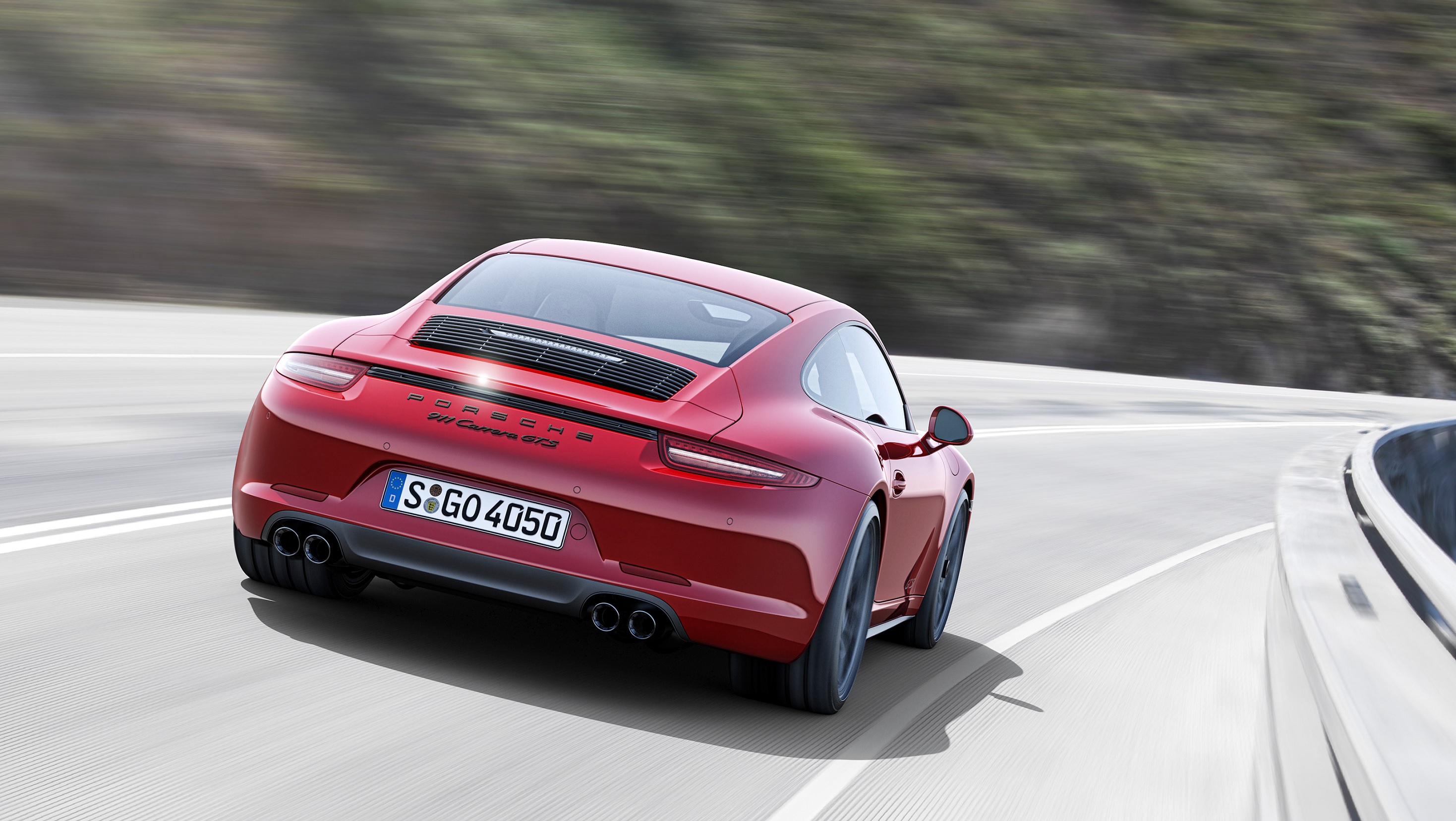 The rear 3/4 view of a red 2015 Porsche 991.1 911 Carrera GTS driving down a canyon road