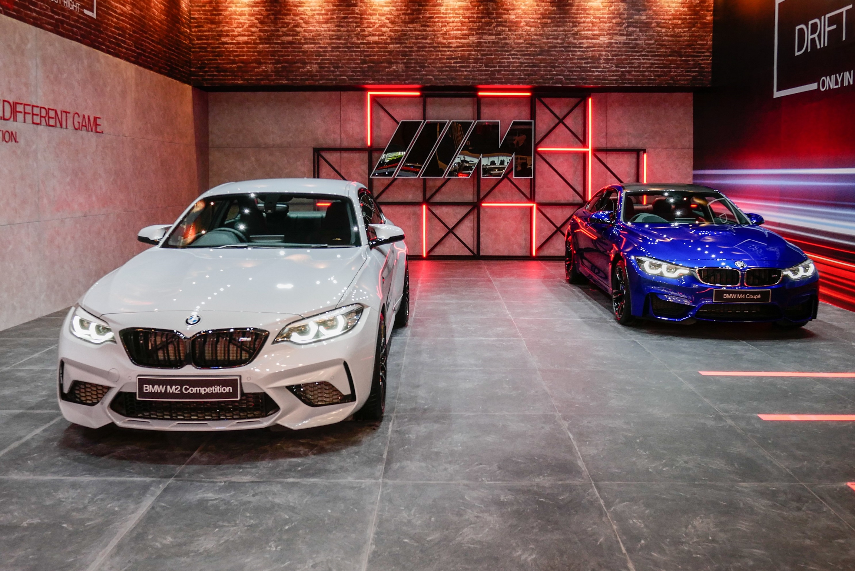 A white 2019 BMW M2 Competition next to a blue 2019 BMW M4 at the 2019 GAIKINDO Indonesia International Auto Show
