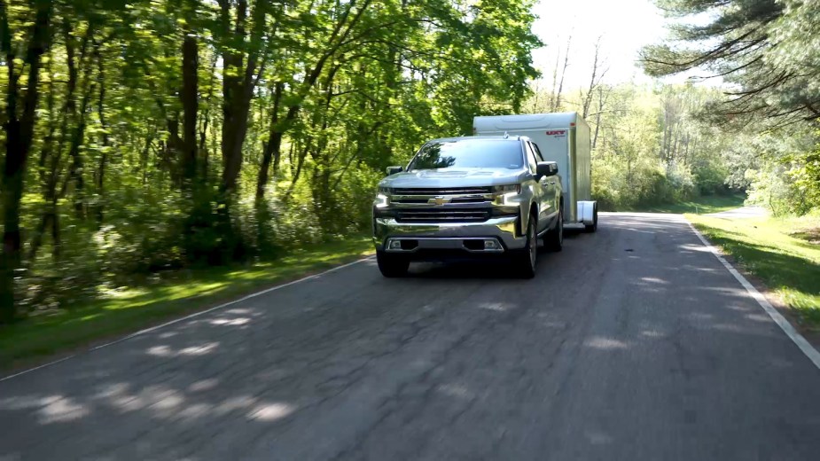 Promo shot of a Silverado 1500 towing a white box trailer down a tree-lined country road.