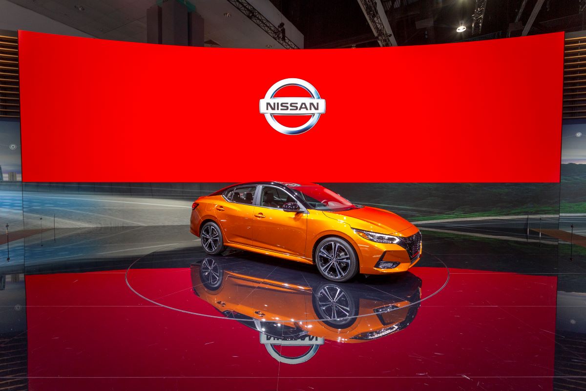 An orange 2019 Nissan Sentra parked in front of a large digital banner at an auto show