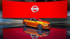 An orange 2019 Nissan Sentra parked in front of a large digital banner at an auto show