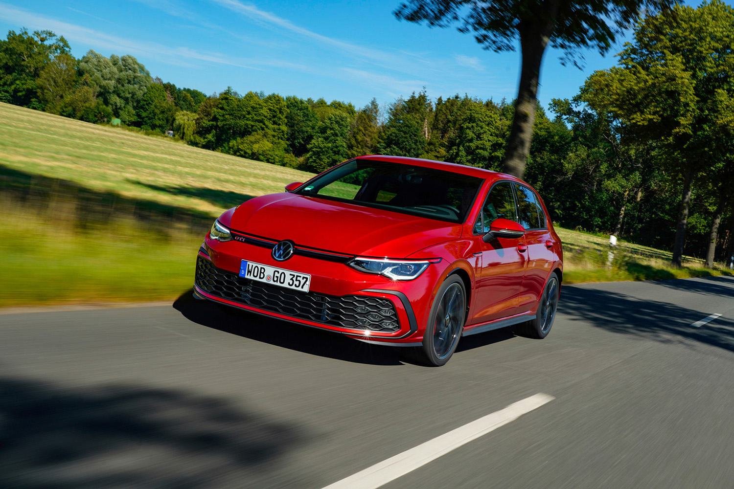 Red 2020 Volkswagen Golf GTI cruising past a grassy field in the sun, the best used compact car to buy