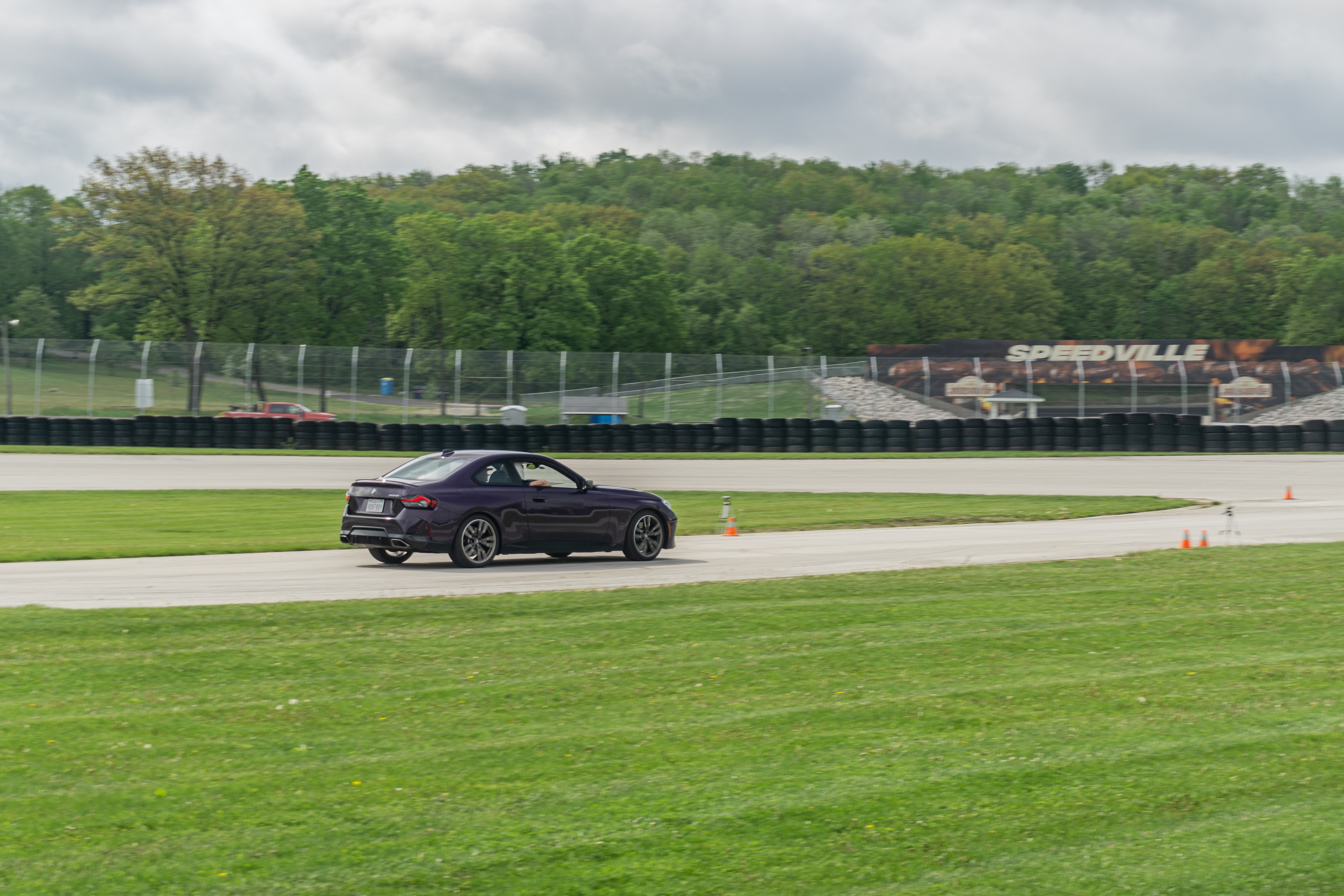 The rear 3/4 view of a purple 2022 BMW M240i xDrive Coupe racing on Road America's autocross course