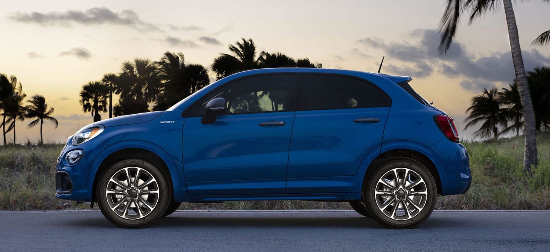 A blue 2022 Fiat 500X subcompact crossover SUV model parked near palm trees at sunset