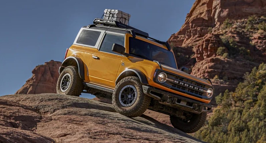 A yellow 2022 Ford Bronco small off-road SUV is driving on a rock.