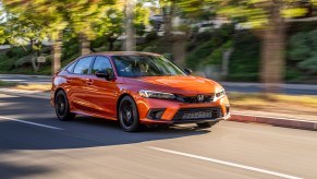 An orange 2022 Honda Civic Si driving on a tree lined street