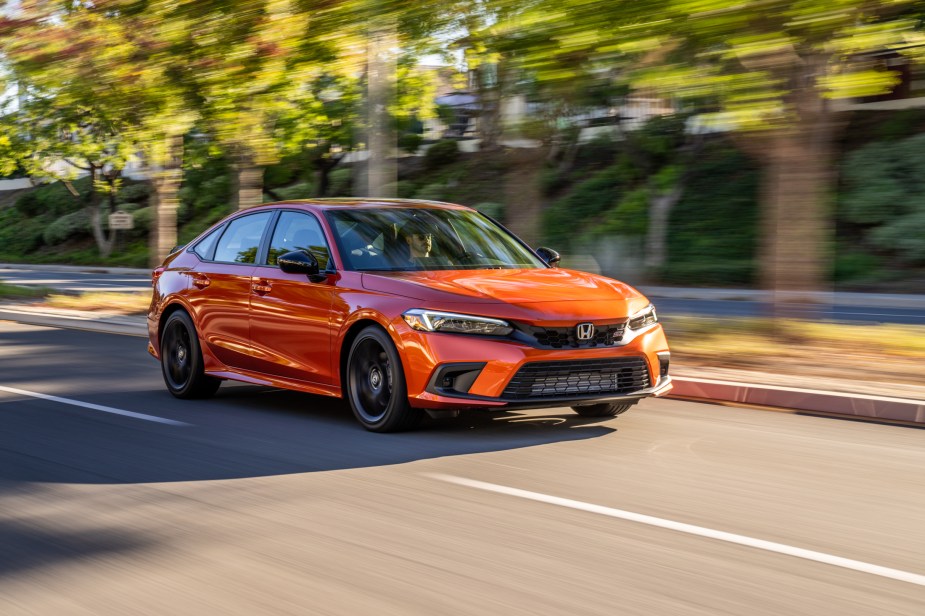 An orange 2022 Honda Civic Si driving on a tree lined street