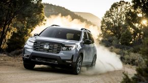 A 2022 Honda Passport Trailsport SUV model driving on a dirt trail as a cloud of kicked up dirt and dust trails it