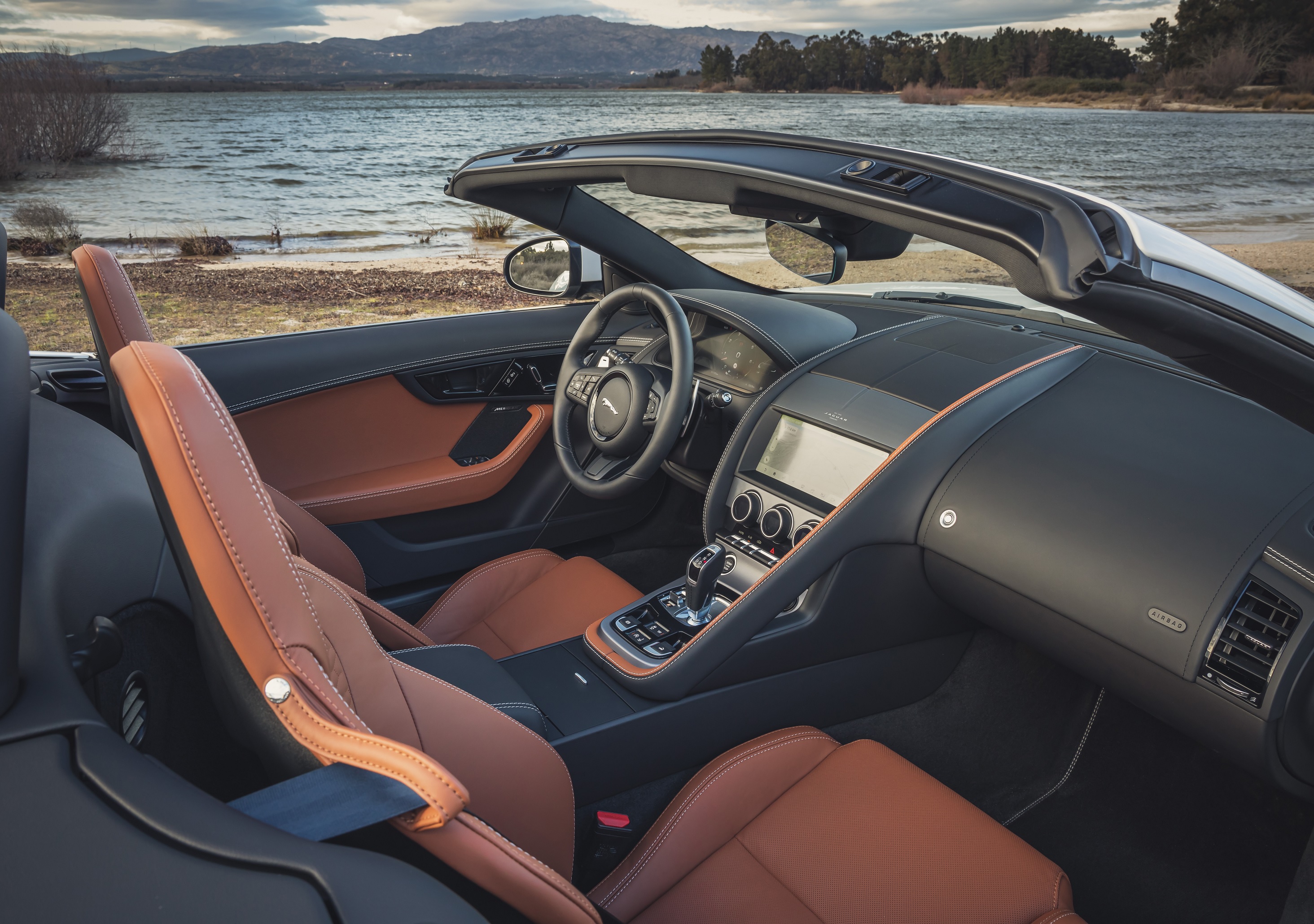 The brown leather seats and black leather dashboard of a 2022 Jaguar F-Type Convertible P450 next to a mountain lake