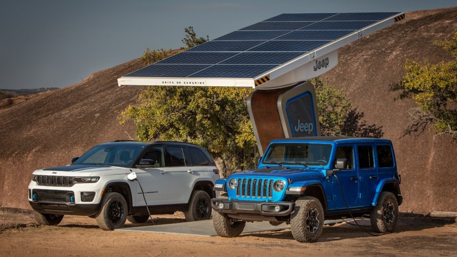 Blue Jeep wrangler and White Grand Cherokee parked side-by-side under a solar panel in the desert.