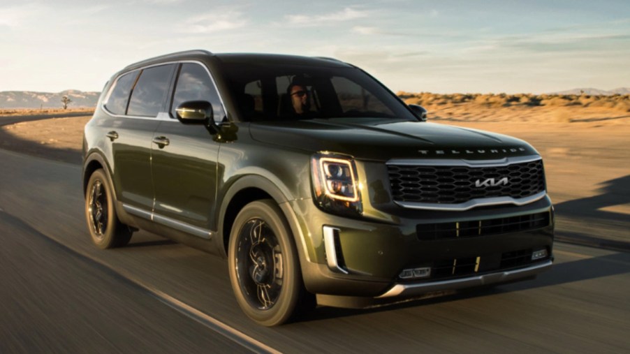 A green 2022 Kia Telluride is driving on the road.