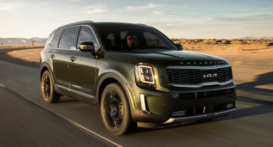 A green 2022 Kia Telluride midsize SUV is driving on the road. 