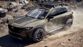 A 2023 Mazda CX-50 compact crossover SUV driving on a dirt road as dust trails around it