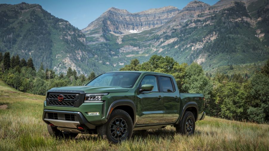 A green 2022 Nissan Frontier compact pickup truck with 9.4 inches of ground clearance parked near a mountain range forest