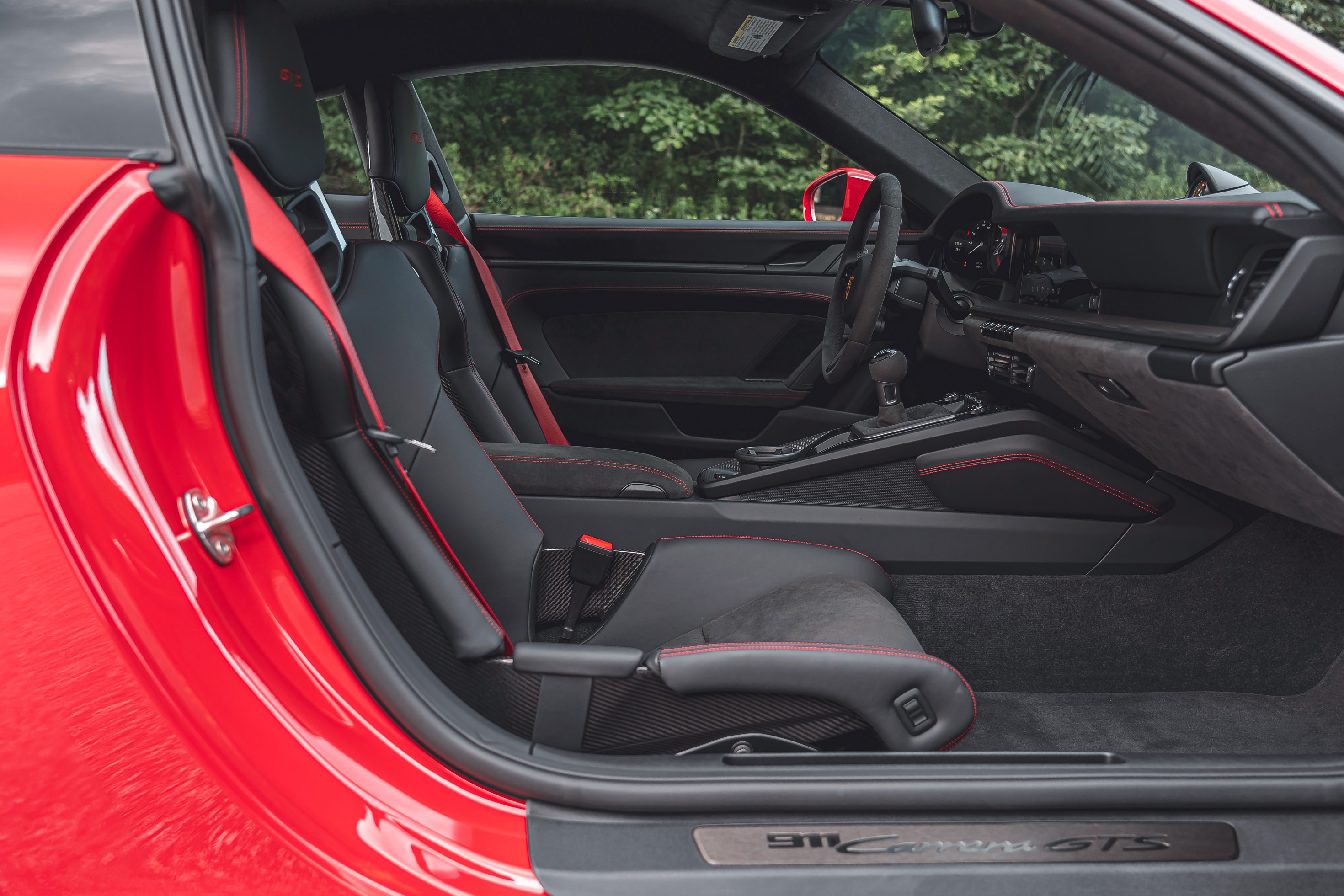 The black and red stitched front sports seats and dashboard of a red 2022 Porsche 911 Carrera GTS