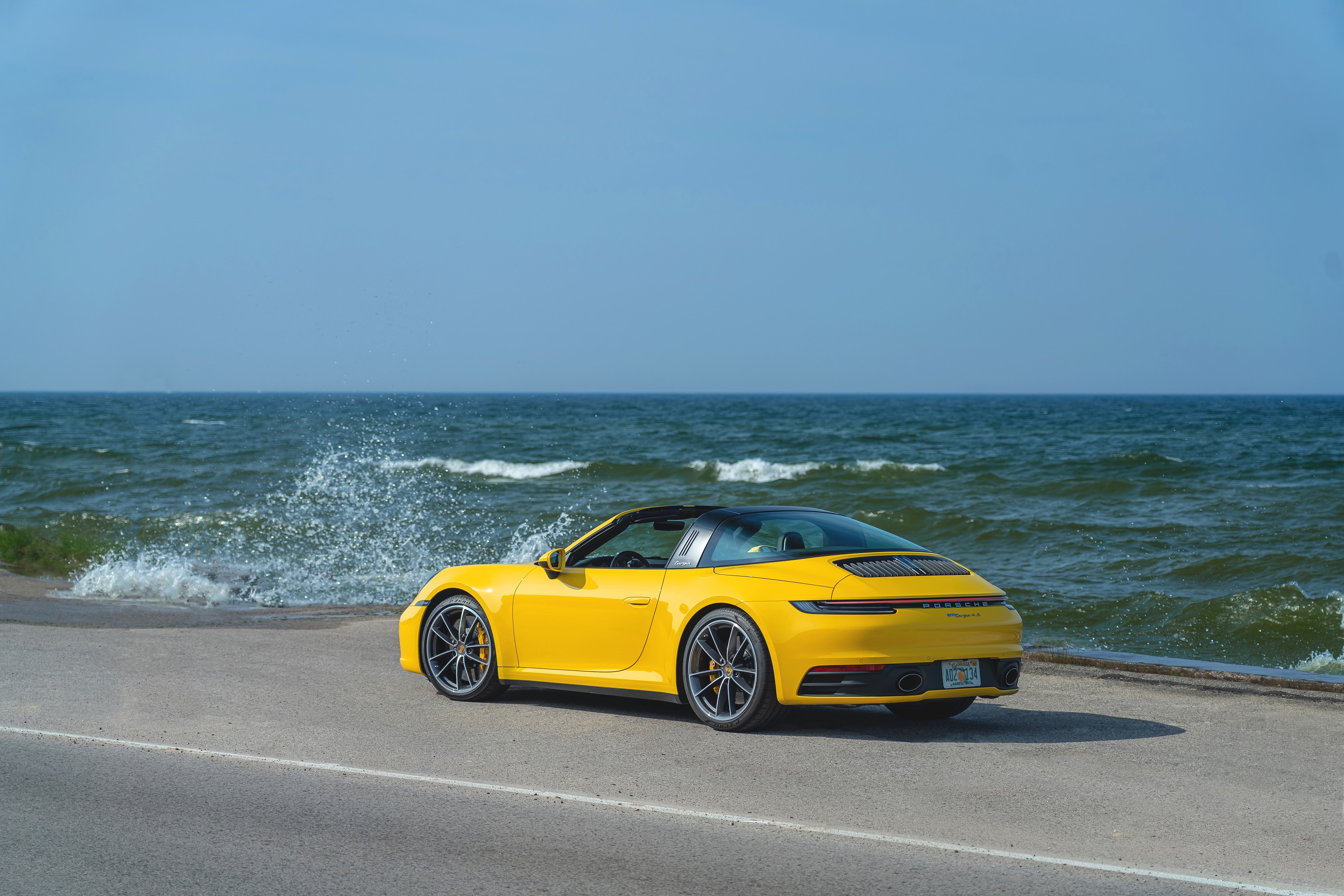 The 3/4 rear view of a yellow 2022 Porsche 911 Targa 4S by the sea