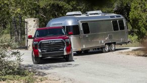 Red Toyota Tundra pickup truck towing an airstream camper trailer down a wooded road.