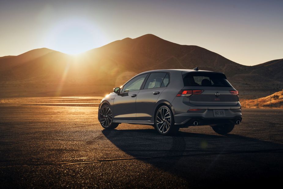 A gray 2022 Volkswagen Golf GTI hot hatchback parked on an asphalt lot as the sunsets behind a hill