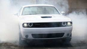 White 2022 Dodge Challenger R/T Scat Pack throwing up smoke from its tires. The 2022 Dodge Challenger has faster acceleration than the 2022 Ford Mustang