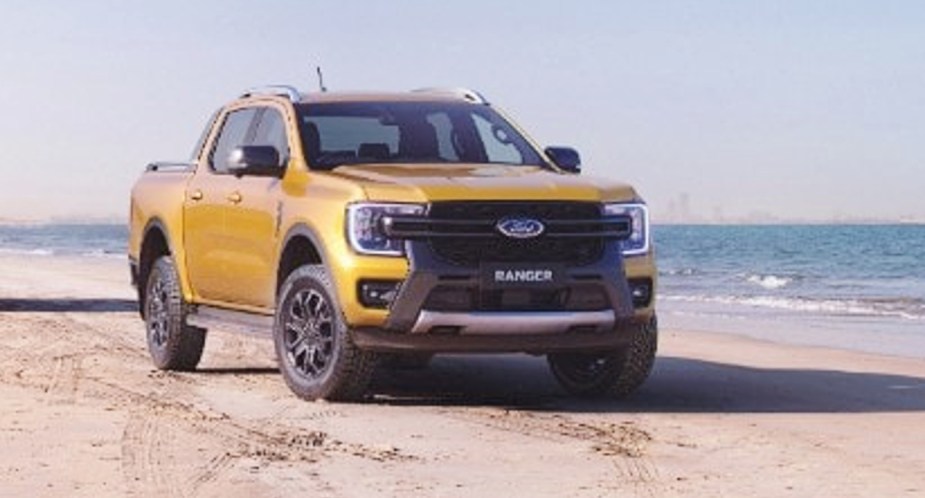 A yellow 2023 Ford Ranger Wildtrak off-road pickup truck is parked on the sand.  