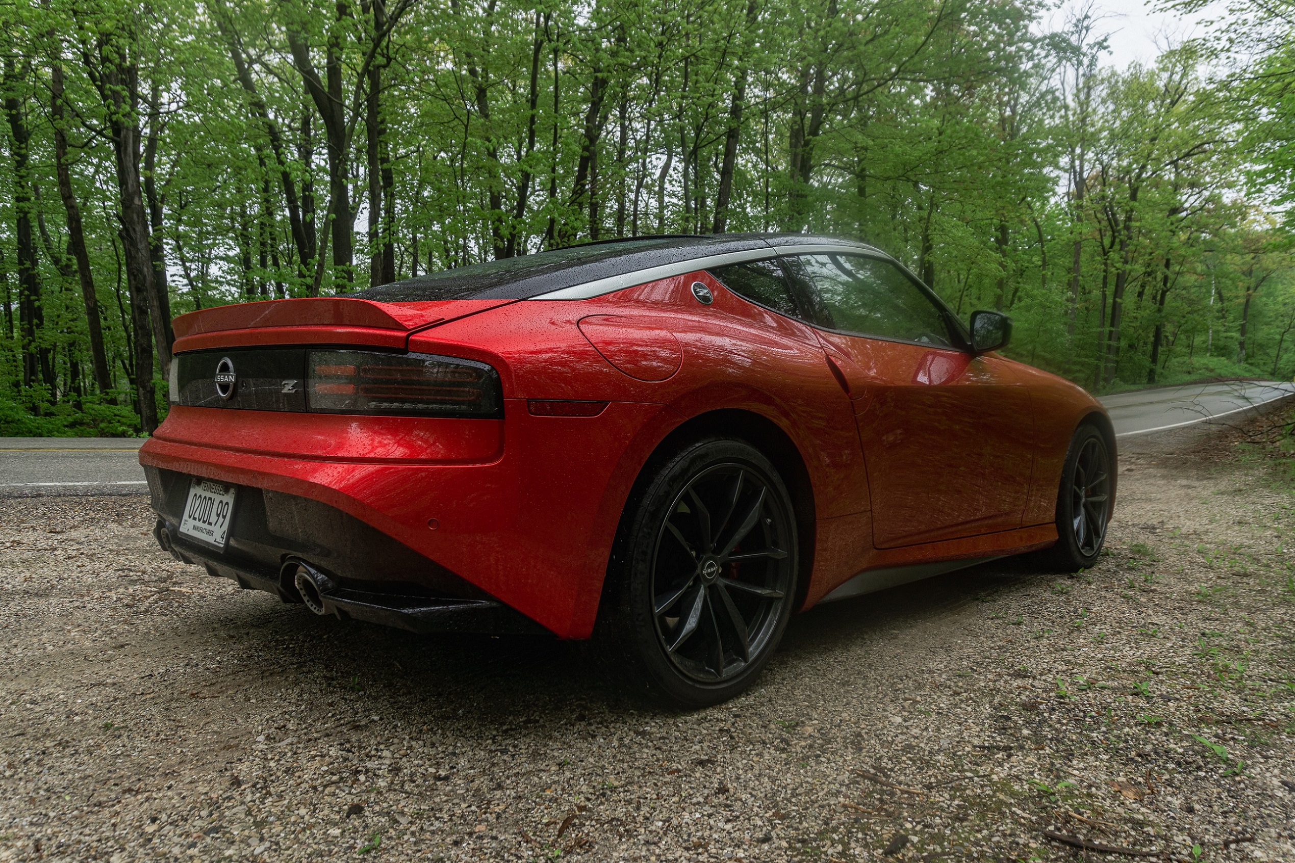 The 3/4 rear view of a red 2023 Nissan Z Performance on a forest road