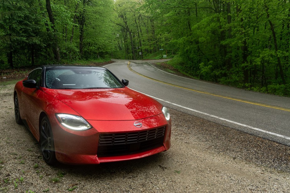 A red 2023 Nissan Z Performance next to a rainy forest road