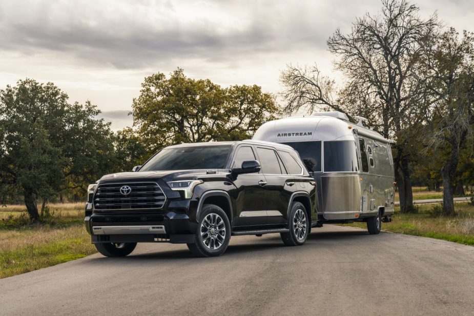 The new 2023 Toyota Sequoia hooked up to an airstream camper trailer, parked on a country road.