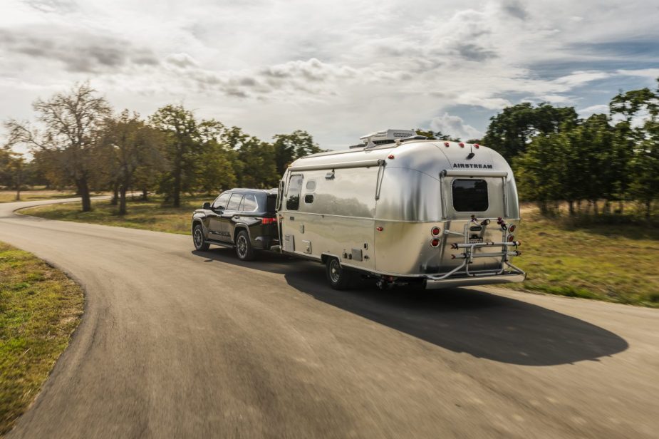 An airstream camper trailer being towed down a tree-lined road by the new 2023 Toyota Sequoia SUV.