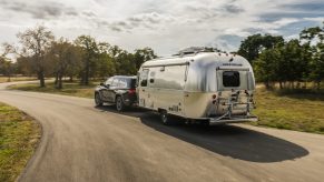 2023 Toyota Sequoia SUV towing an airstream camper trailer down a curvy, tree-lined road.