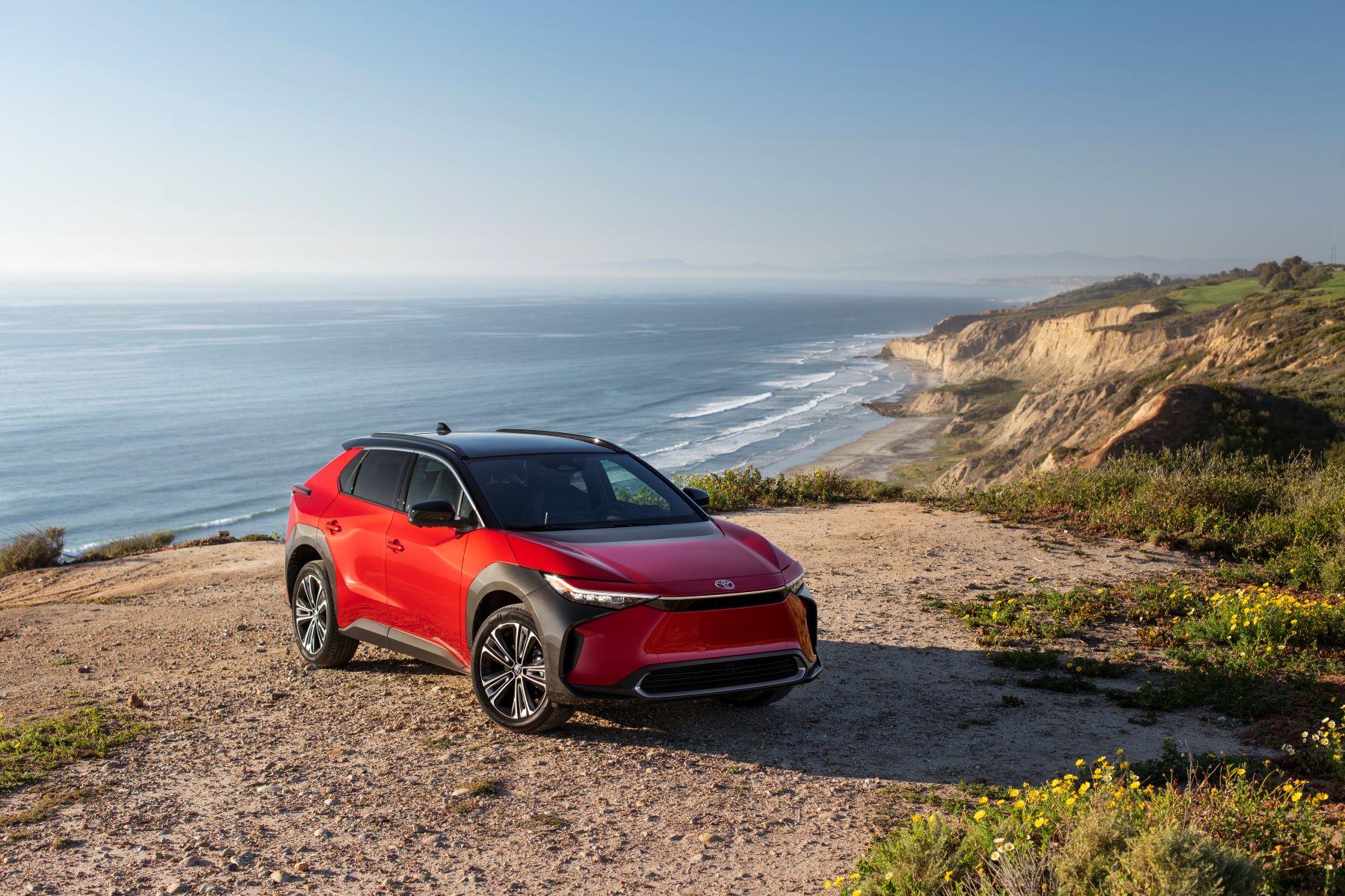 A red 2023 Toyota bZ4X Limited AWD electric SUV model parked on a sandy cliff near a seaside of crashing waves