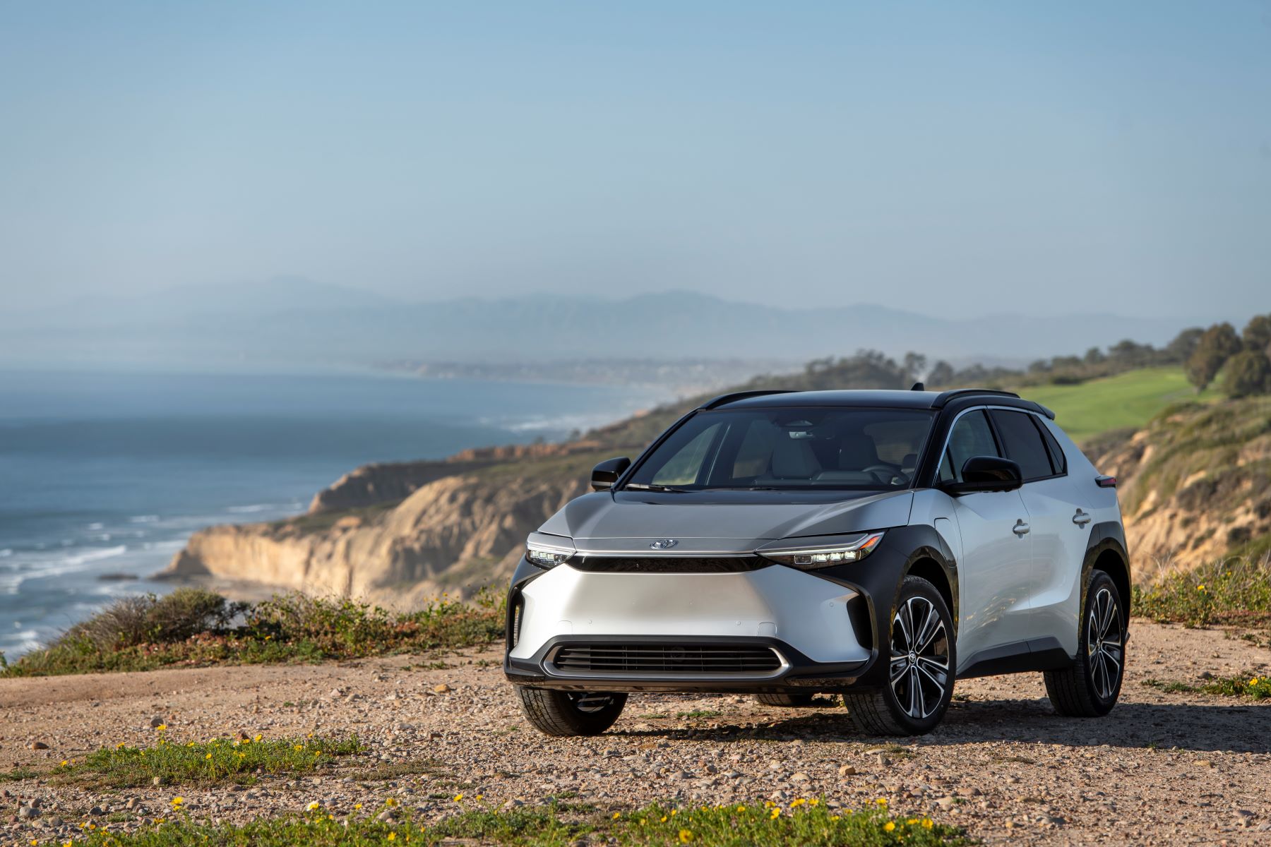 A 2023 Toyota bZ4X Limited EV/electric SUV model in Elemental Silver Metallic parked on a cliff near crashing waves