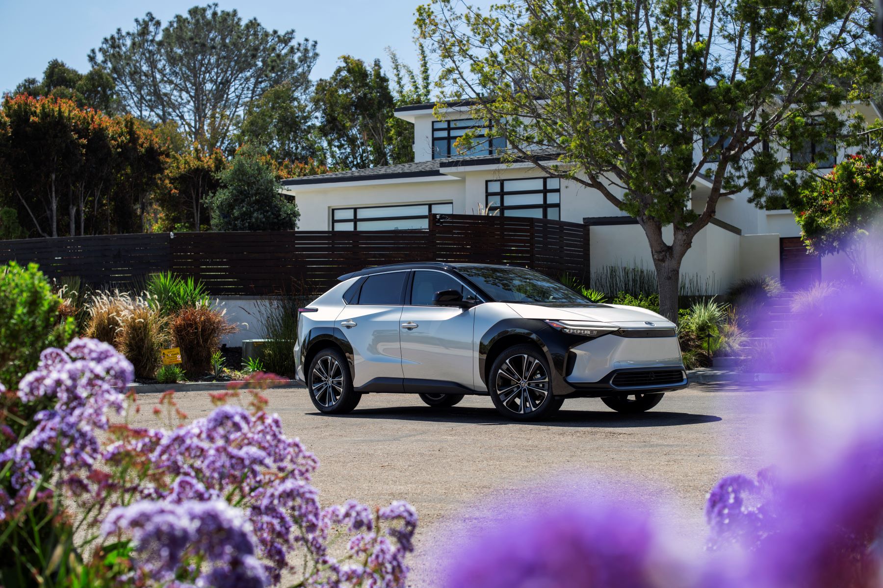 A 2023 Toyota bZ4X Limited EV/electric SUV model in Elemental Silver Metallic farmed by lavender flowers outside a house