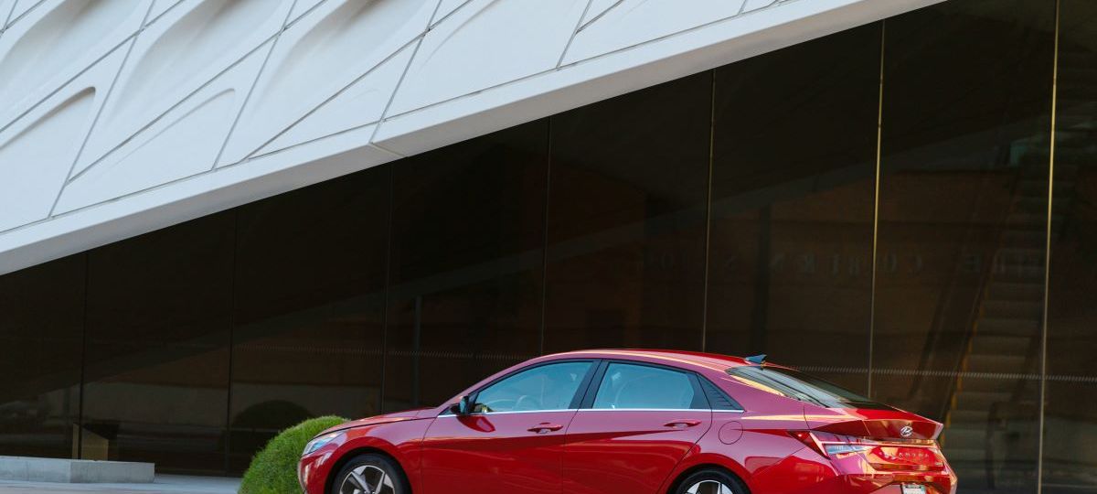 Red 2023 Hyundai Elantra midsize sedan parked in front a modern-looking building