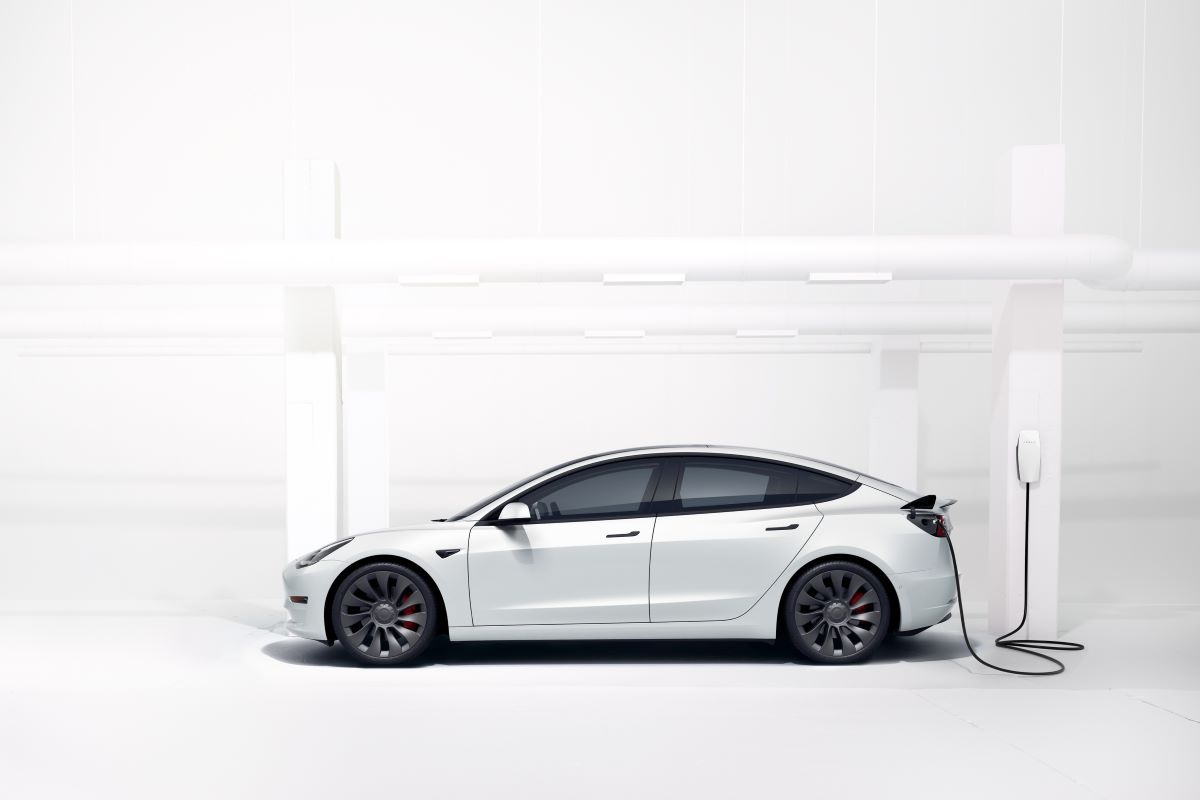 A white 2023 Tesla Model 3 plugged into a charging station set against a crisp white background
