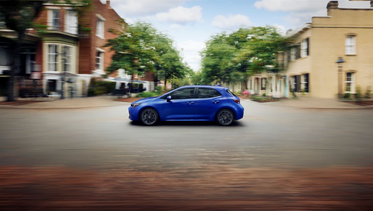 Side view of a blue 2023 Toyota Corolla Hatchback driving along an empty city road