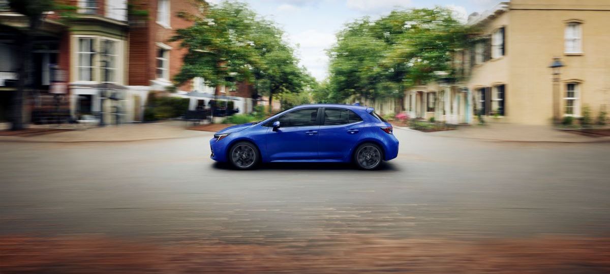 Side view of a blue 2023 Toyota Corolla Hatchback driving along an empty city road