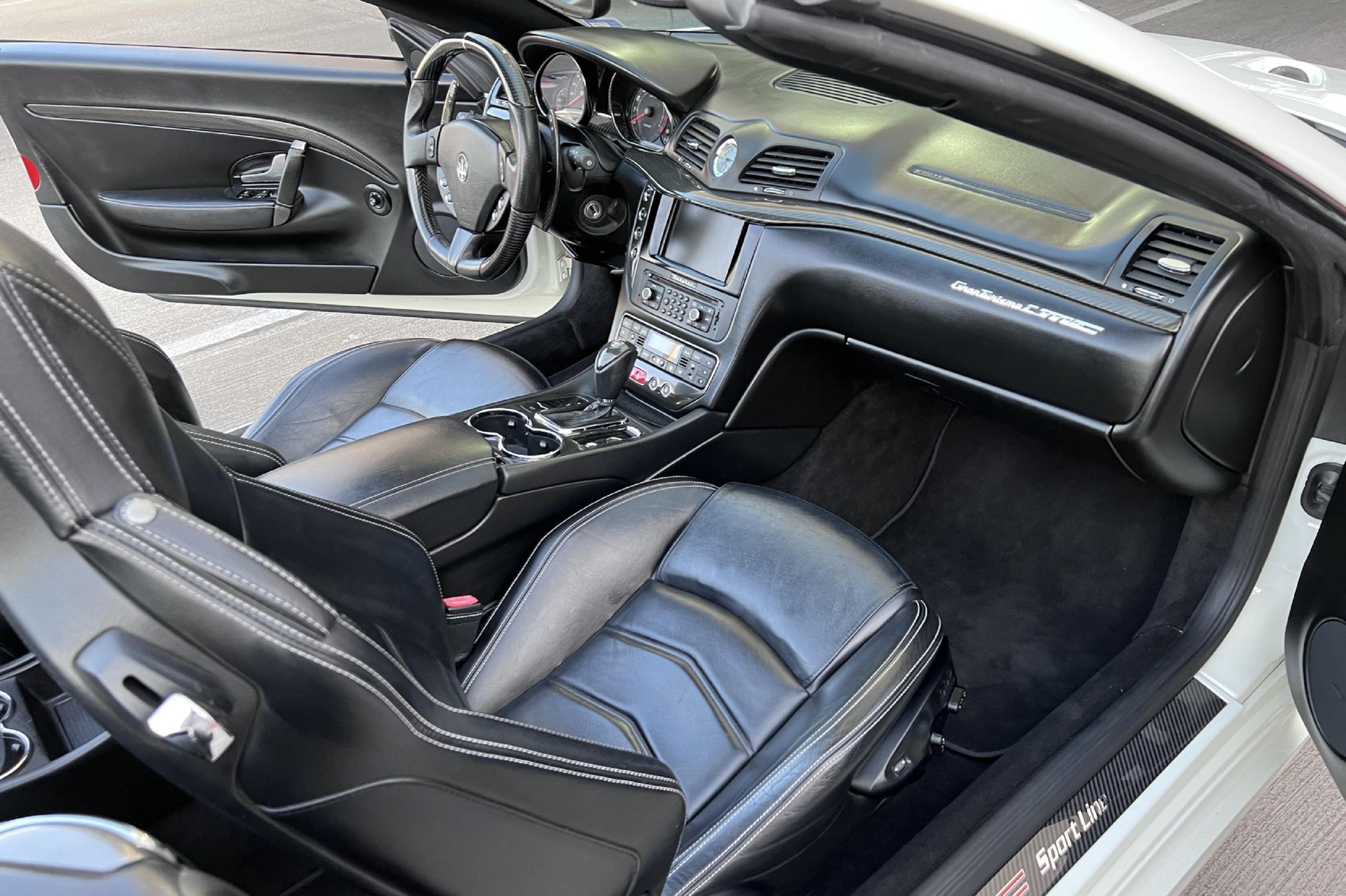 The black leather seats and carbon fiber clad black dashboard of a white 2013 Maserati GranTurismo MC Convertible
