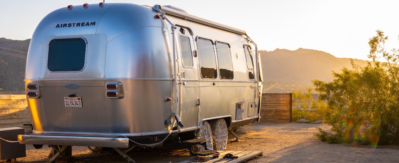 Silver Airstream camper trailer, with the sun setting over mountains in the background.